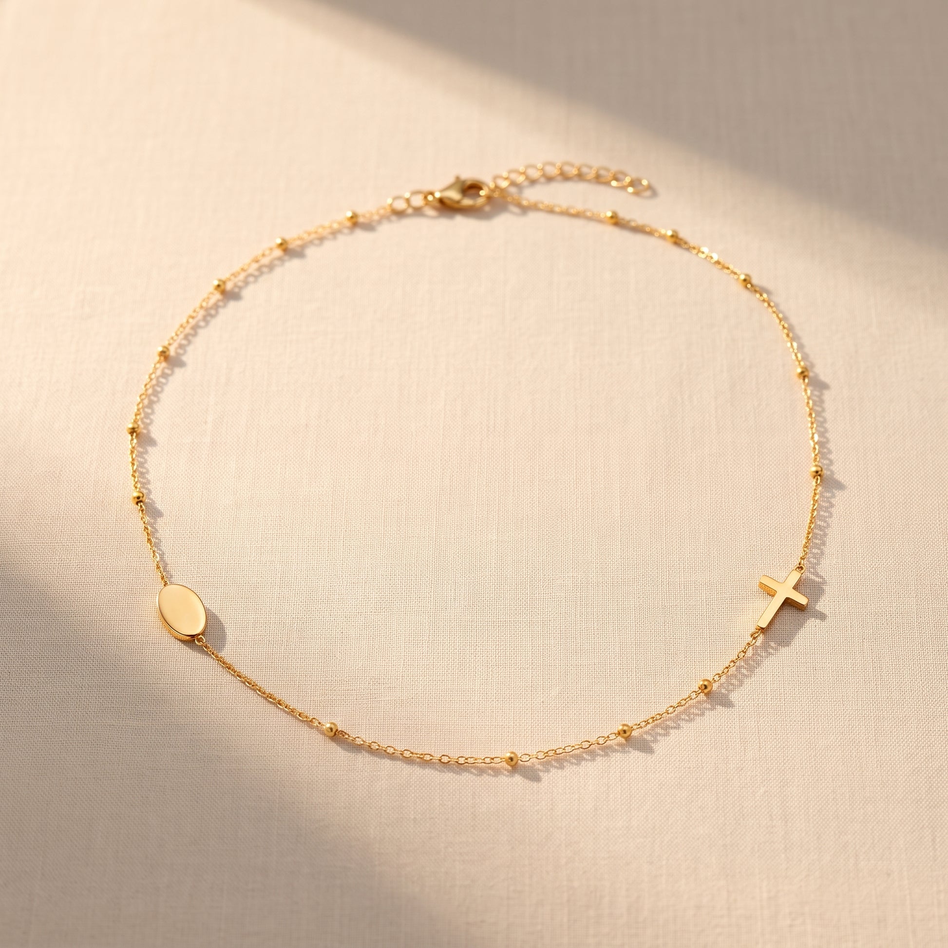 Collar Fe Serena de acabado dorado con cadena satelital, disco liso y cruz pequeña, sobre fondo de lino