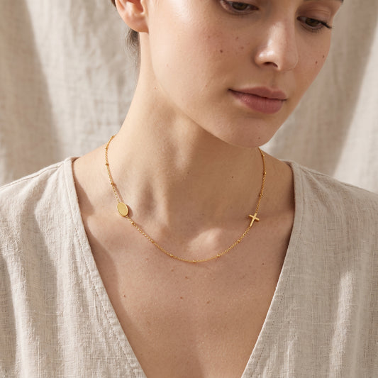 Mujer luciendo un collar con cadena dorada fina con disco liso y cruz minimalista