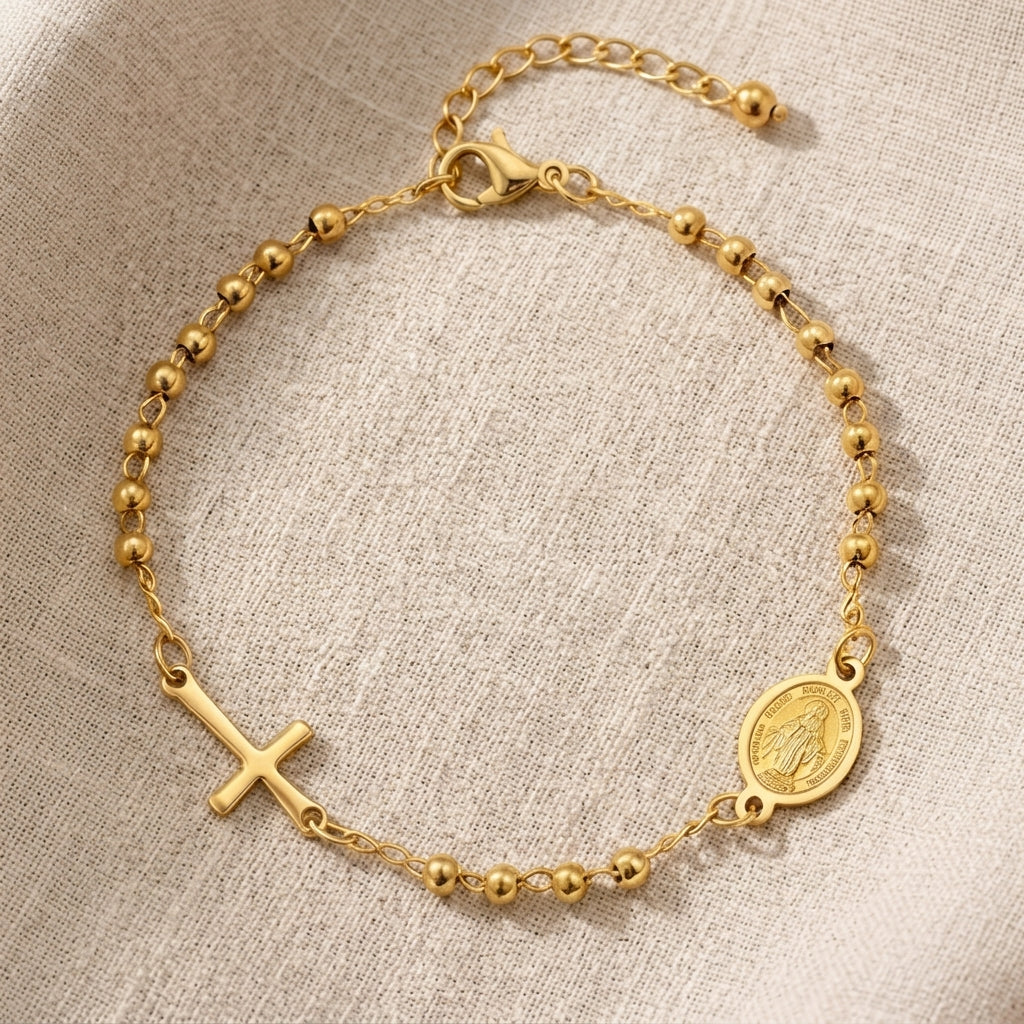 Detalle de pulsera dorada con cruz y medalla mariana, joyería Aura Sacra