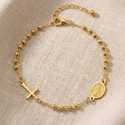 Detalle de pulsera dorada con cruz y medalla mariana, joyería Aura Sacra