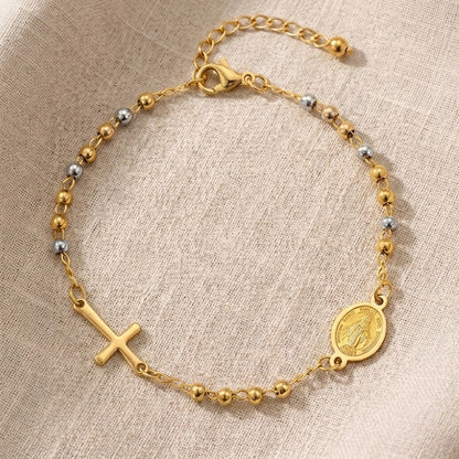 Detalle de pulsera dorada y plateada con cruz y medalla mariana, joyería Aura Sacra
